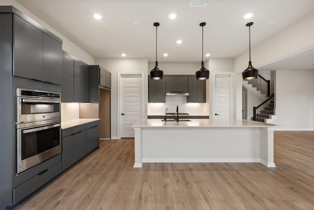 kitchen featuring gray cabinetry, stainless steel double oven, tasteful backsplash, decorative light fixtures, and light wood-type flooring