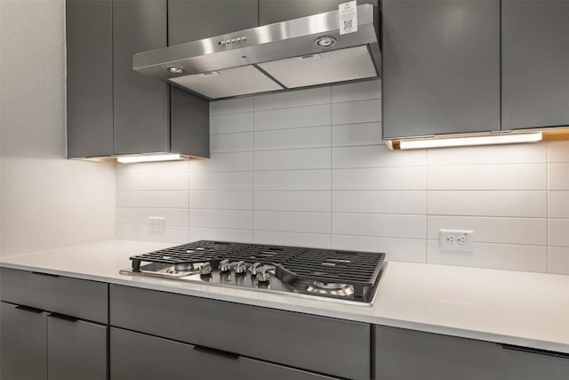 kitchen featuring backsplash, stainless steel gas cooktop, gray cabinetry, and range hood