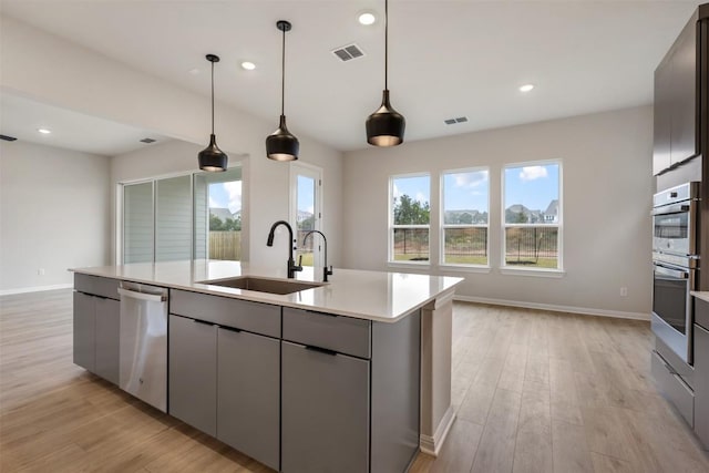 kitchen featuring sink, stainless steel appliances, light hardwood / wood-style flooring, decorative light fixtures, and a kitchen island with sink