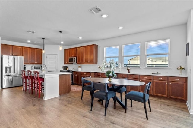 kitchen with a kitchen bar, stainless steel appliances, decorative light fixtures, a center island with sink, and light hardwood / wood-style floors