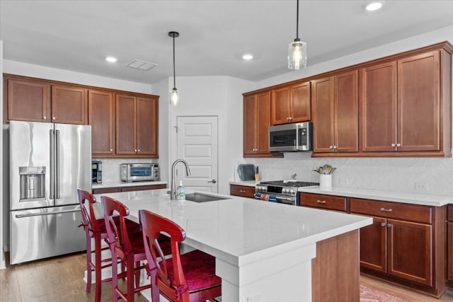 kitchen with sink, stainless steel appliances, a kitchen breakfast bar, pendant lighting, and a kitchen island with sink