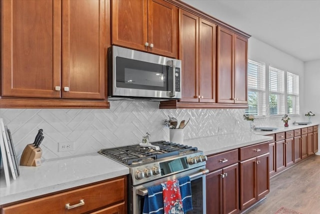 kitchen with tasteful backsplash, light stone countertops, light hardwood / wood-style flooring, and appliances with stainless steel finishes