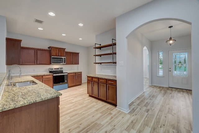 kitchen featuring tasteful backsplash, stainless steel appliances, sink, pendant lighting, and light hardwood / wood-style flooring