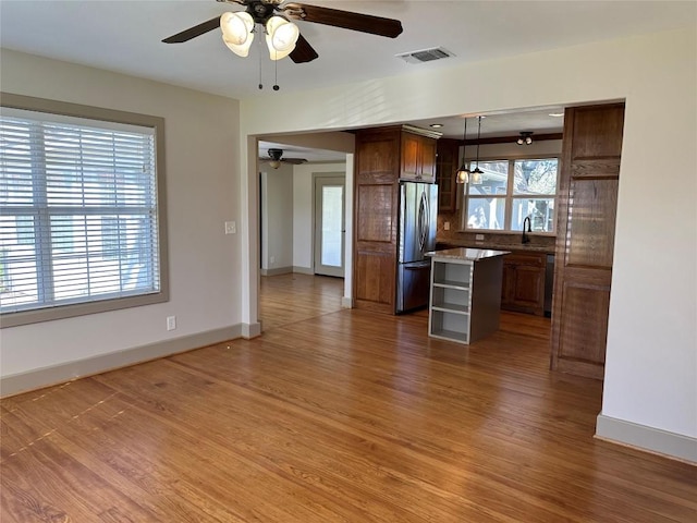 kitchen featuring decorative light fixtures, a kitchen island, a wealth of natural light, and stainless steel refrigerator