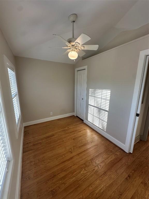 unfurnished bedroom featuring multiple windows, hardwood / wood-style flooring, vaulted ceiling, and ceiling fan