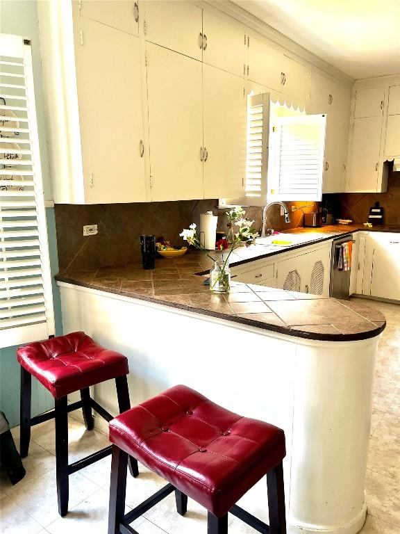 kitchen featuring tile countertops, sink, stainless steel dishwasher, decorative backsplash, and white cabinetry