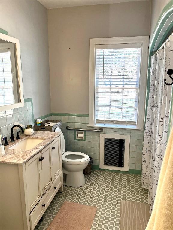 bathroom with a shower with curtain, vanity, heating unit, tile walls, and toilet