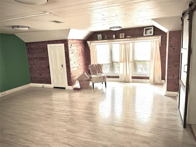 additional living space with a barn door, lofted ceiling, wooden walls, and light hardwood / wood-style flooring