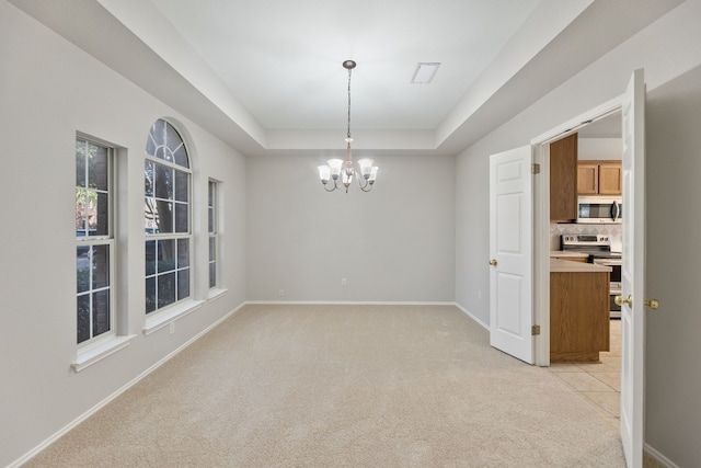 carpeted spare room featuring a raised ceiling and a chandelier