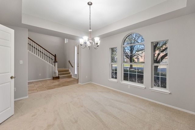 spare room featuring a tray ceiling, light colored carpet, and a notable chandelier