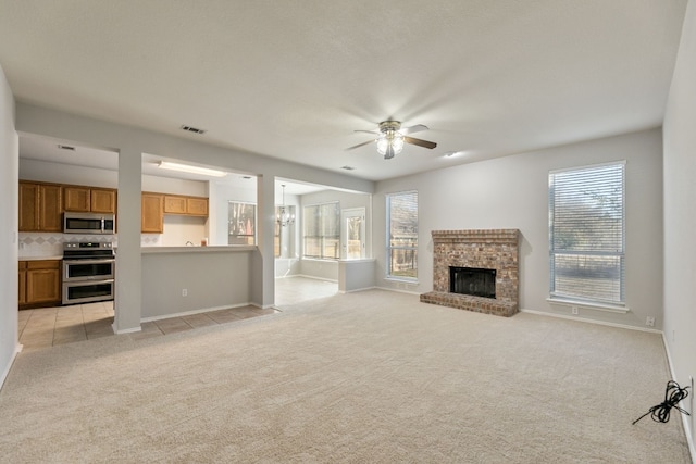 unfurnished living room featuring light colored carpet, ceiling fan with notable chandelier, and a brick fireplace