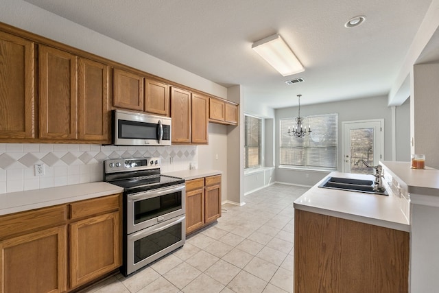 30004 Oakland Hills Dr, Georgetown, TX 78628 - kitchen with appliances with stainless steel finishes, brown cabinetry, a chandelier, and backsplash