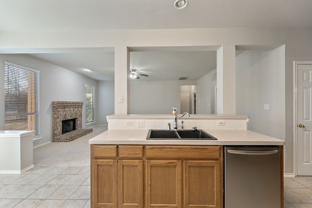 kitchen with ceiling fan, sink, a brick fireplace, stainless steel dishwasher, and an island with sink