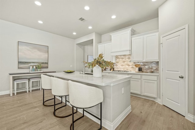 kitchen featuring white cabinets, a kitchen island with sink, stainless steel gas cooktop, and light hardwood / wood-style flooring