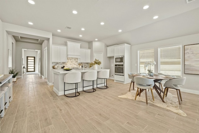 kitchen featuring a breakfast bar, lofted ceiling, oven, an island with sink, and white cabinetry