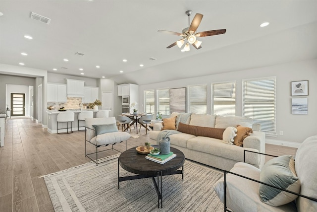 living room with ceiling fan, light wood-type flooring, and lofted ceiling