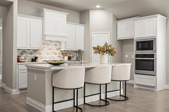 kitchen with built in microwave, oven, a center island with sink, and white cabinets