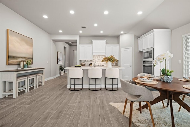 kitchen featuring built in microwave, white cabinetry, a kitchen breakfast bar, stainless steel oven, and a center island with sink