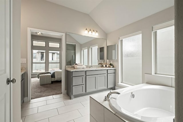 bathroom with vanity, tile patterned flooring, vaulted ceiling, and tiled tub