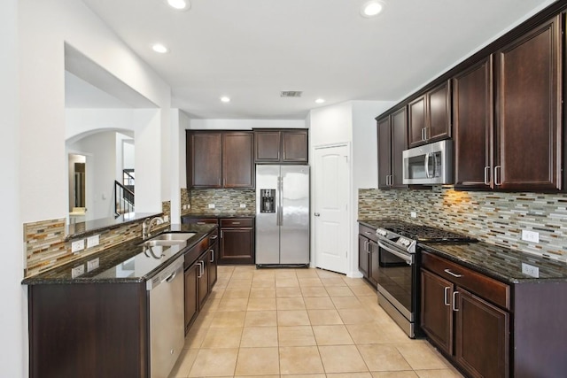 kitchen with sink, stainless steel appliances, tasteful backsplash, dark stone countertops, and light tile patterned flooring