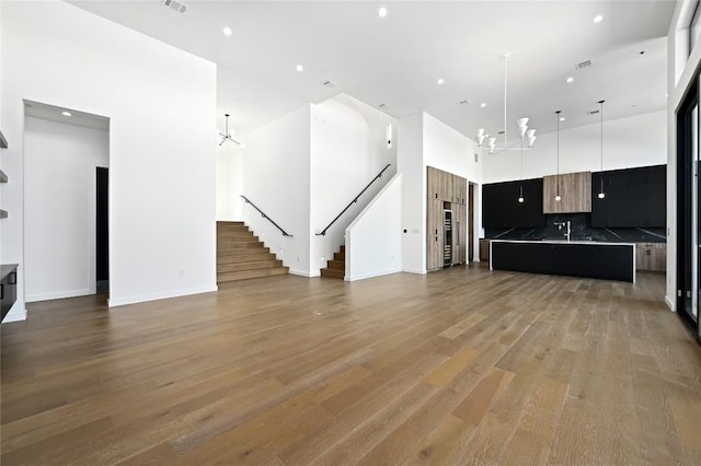 kitchen with a high ceiling, tasteful backsplash, a notable chandelier, wood-type flooring, and a center island with sink