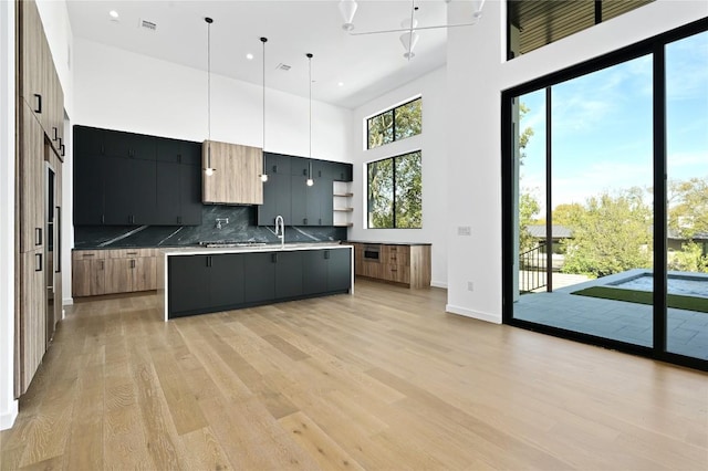 kitchen with decorative light fixtures, plenty of natural light, decorative backsplash, and a kitchen island with sink