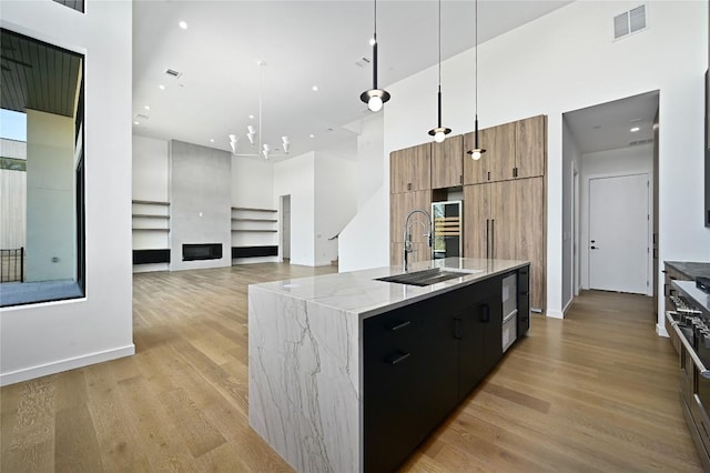 kitchen featuring a kitchen island with sink, a high ceiling, sink, decorative light fixtures, and a chandelier