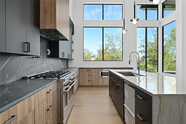 kitchen featuring sink, wall chimney range hood, dark stone countertops, a center island with sink, and appliances with stainless steel finishes