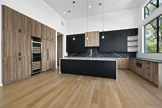 kitchen featuring pendant lighting, a kitchen island with sink, a high ceiling, sink, and tasteful backsplash