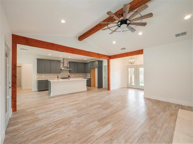 unfurnished living room with ceiling fan with notable chandelier, french doors, light wood-type flooring, and lofted ceiling with beams