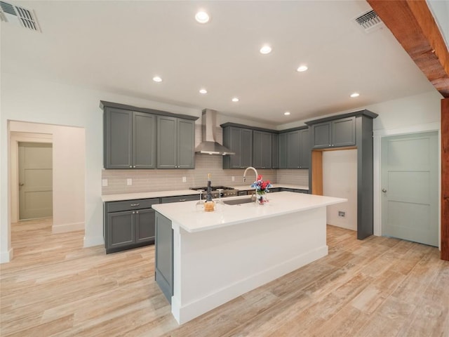 kitchen featuring gray cabinetry, sink, wall chimney exhaust hood, and an island with sink