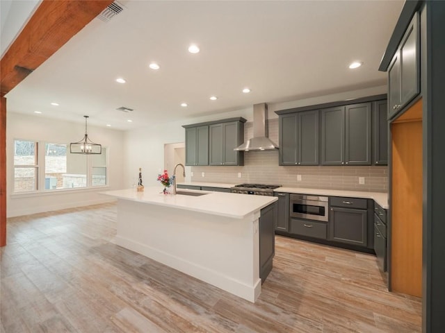 kitchen featuring a center island with sink, hanging light fixtures, light hardwood / wood-style flooring, wall chimney exhaust hood, and built in microwave