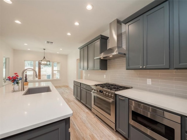 kitchen featuring built in microwave, sink, wall chimney exhaust hood, decorative light fixtures, and high end range