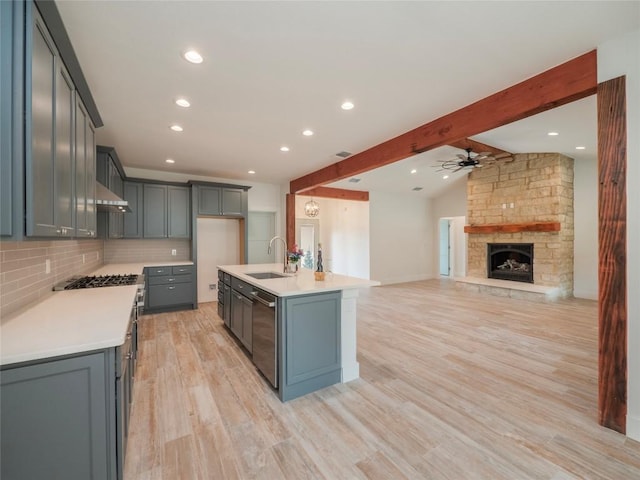 kitchen with a stone fireplace, sink, ceiling fan, an island with sink, and light hardwood / wood-style floors