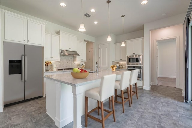 kitchen with a kitchen breakfast bar, an island with sink, decorative backsplash, white cabinets, and appliances with stainless steel finishes