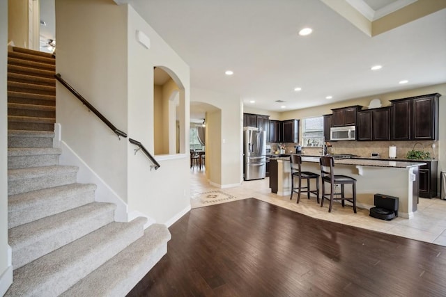 kitchen featuring dark brown cabinetry, backsplash, a breakfast bar area, a kitchen island, and appliances with stainless steel finishes