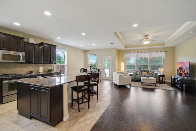 kitchen with a kitchen bar, stainless steel appliances, a raised ceiling, sink, and an island with sink