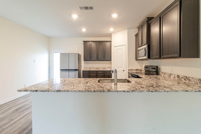 kitchen with sink, light stone countertops, appliances with stainless steel finishes, dark brown cabinets, and kitchen peninsula