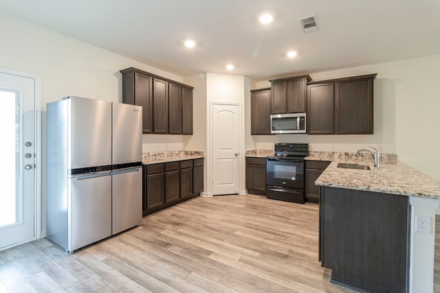 kitchen with sink, stainless steel appliances, light stone counters, light hardwood / wood-style floors, and dark brown cabinets