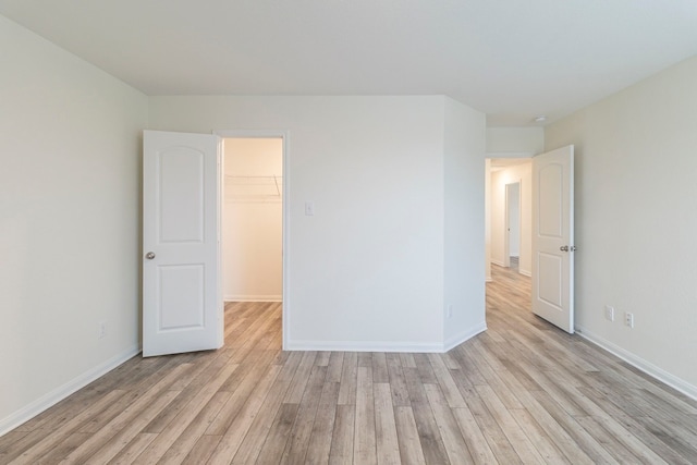 unfurnished bedroom featuring a spacious closet, a closet, and light hardwood / wood-style floors