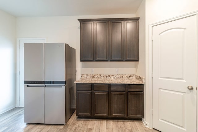 kitchen featuring stainless steel fridge, light wood-type flooring, light stone counters, and dark brown cabinetry