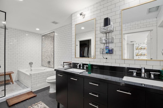 bathroom with tile patterned flooring, tiled tub, toilet, vanity, and tile walls