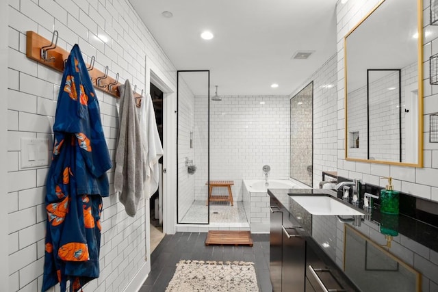 bathroom with plus walk in shower, vanity, tile patterned floors, and tile walls