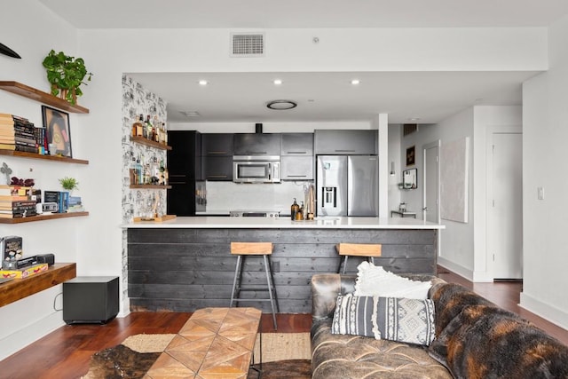 kitchen with a kitchen breakfast bar, dark hardwood / wood-style flooring, kitchen peninsula, and appliances with stainless steel finishes