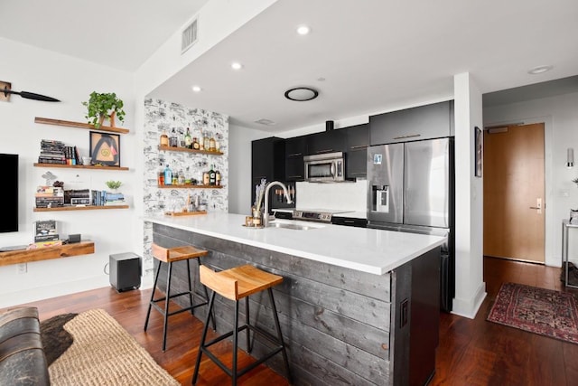 kitchen with stainless steel appliances, dark wood-type flooring, sink, a breakfast bar area, and an island with sink