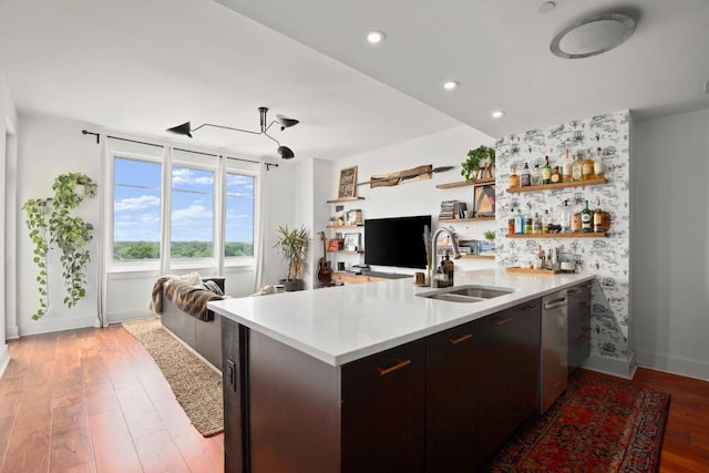 kitchen featuring kitchen peninsula, stainless steel dishwasher, dark brown cabinets, sink, and light hardwood / wood-style flooring