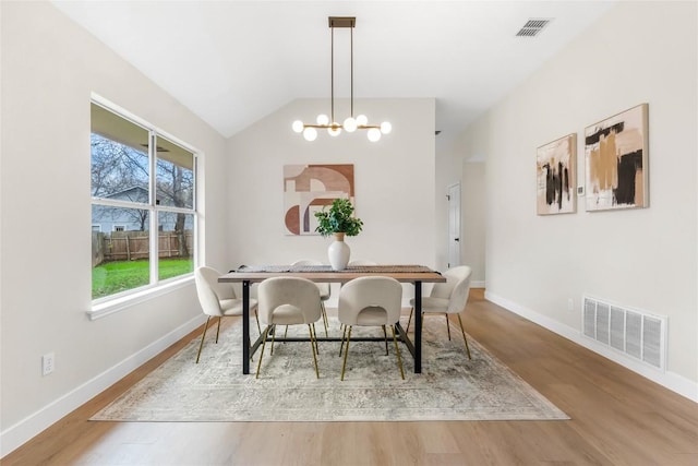 dining room with hardwood / wood-style floors, lofted ceiling, and an inviting chandelier