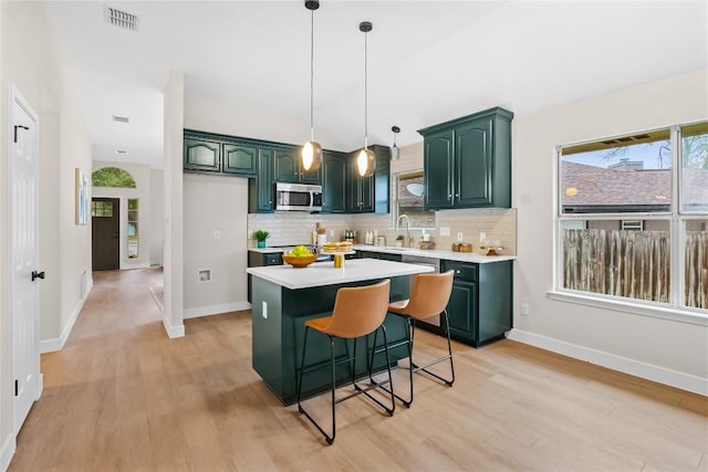 kitchen with sink, light hardwood / wood-style flooring, decorative backsplash, decorative light fixtures, and a kitchen island