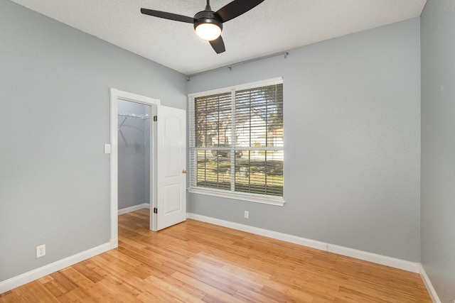 unfurnished bedroom with a walk in closet, light hardwood / wood-style flooring, ceiling fan, a textured ceiling, and a closet