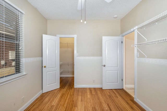 unfurnished bedroom featuring a walk in closet, a textured ceiling, ceiling fan, light hardwood / wood-style flooring, and a closet